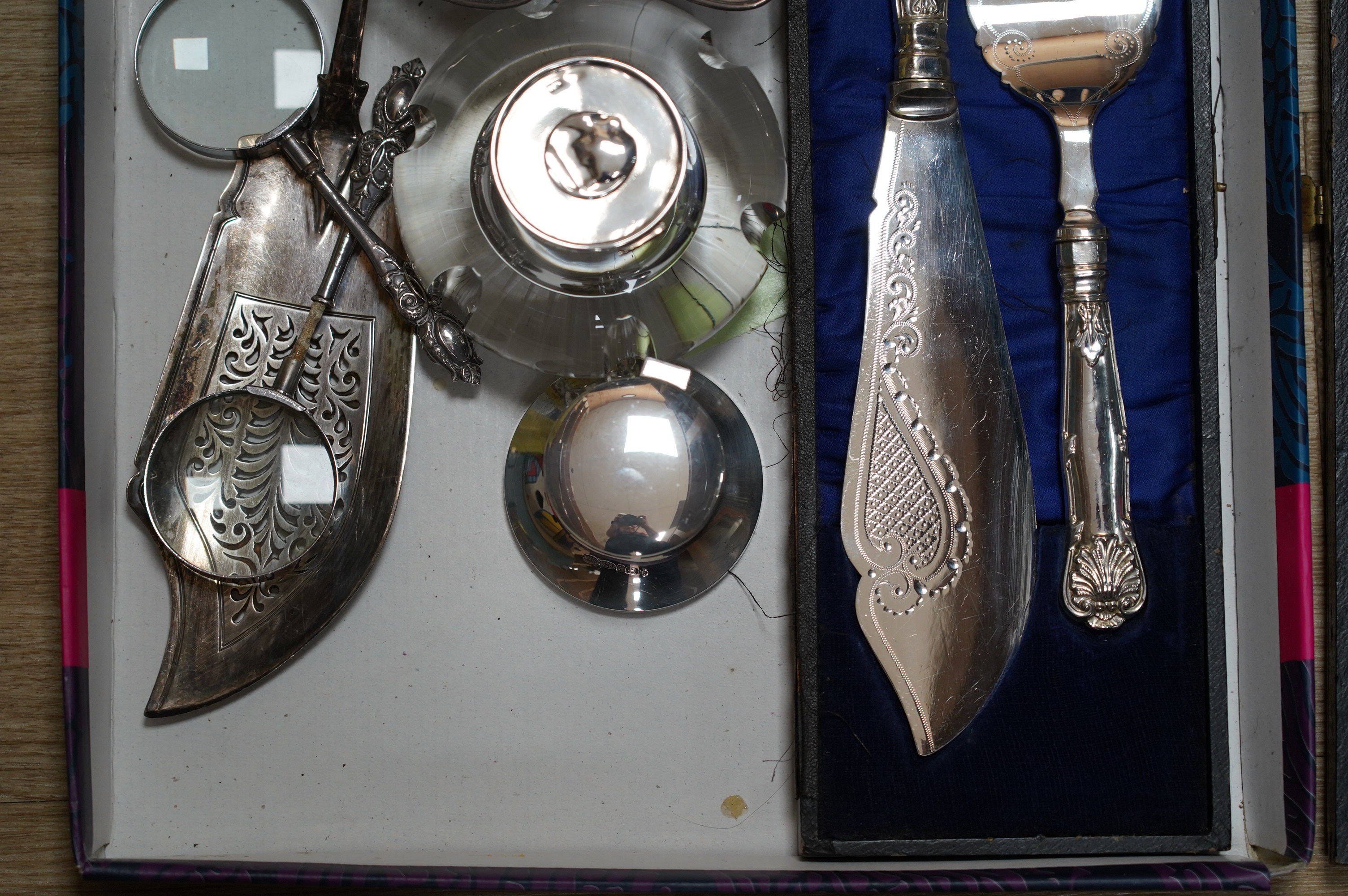 Sundry silver items including two inkwells, a William IV fiddle pattern fish slice, a pair of bonbon dishes and two handled magnifying glasses (one a.f.), together with a cased pair of plated fish servers. Condition - po
